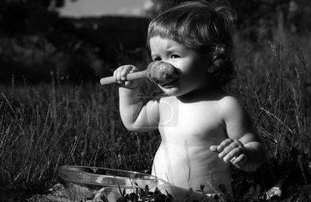Photo for Funny baby in park eats herself with big wooden spoon. Blurred nature background. Healthy eating for kids. Child nutrition - Royalty Free Image