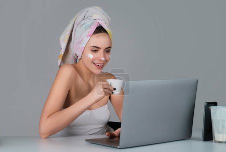 Téléchargez les photos : Morning woman with coffee and facial mask on daily routine. Enjoying time at home. Beautiful young smiling woman working on laptop and drinking coffee - en image libre de droit