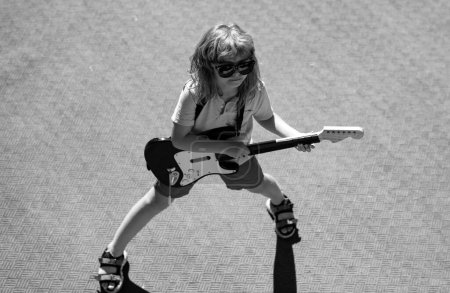 Téléchargez les photos : Petit garçon jouant de la guitare en plein air. Enfant musicien guitariste jouant de la guitare électrique. Musique pour enfants - en image libre de droit