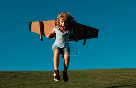 Foto de Funny Child saltando y corriendo con una mochila de juguete. Niño piloto astronauta o astronauta sueña con volar. Aviador volando con alas de cartón - Imagen libre de derechos