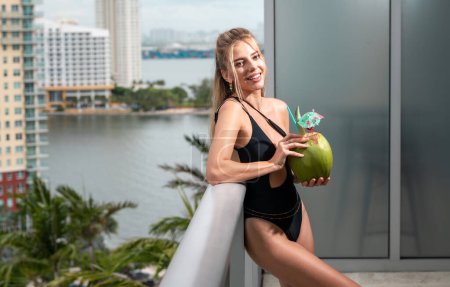 Foto de Joven mujer sonriente en traje de baño con coco. Vacaciones de verano en Miami. Bebida de coco. Vacaciones de viaje tropical. Descanso en vila de lujo y resort - Imagen libre de derechos
