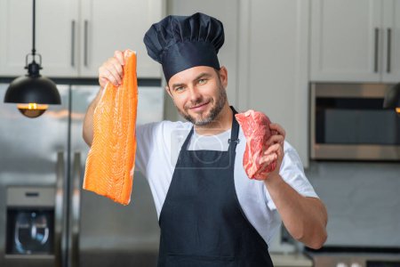 Foto de Salud, proteína natural. Hombre guapo en la cocina cocinando pescado y carne, salmón y carne de res en la cocina. Concepto de comida saludable. Dieta saludable, proteína de carne. Pescado y carne crudos - Imagen libre de derechos