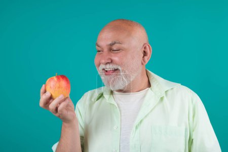 Téléchargez les photos : Grand-père aîné mange des pommes en studio. Portrait d'un homme âgé mangeant une pomme. Un homme qui mord des pommes. Pommes pour personnes âgées. Senior sur l'alimentation et un mode de vie sain. Portrait studio senior avec pommes - en image libre de droit