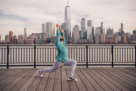 Foto de Hombre en ropa deportiva haciendo ejercicio cerca de Manhattan. Ejercicios saludables. Hombre mayor activo es ejercicio de fitness al aire libre. Ejercicio después de la jubilación. Maduro deportista retirado haciendo ejercicios de estiramiento - Imagen libre de derechos
