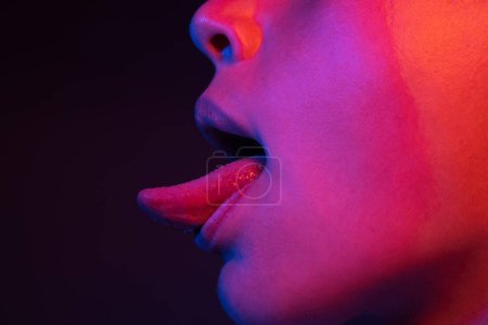 Foto de Lame la lengua. Sexy boca de mujer con la lengua sobresaliendo. Lengua sexy. Se acabó la lengua. Luz de neón, escena sexy de noche - Imagen libre de derechos