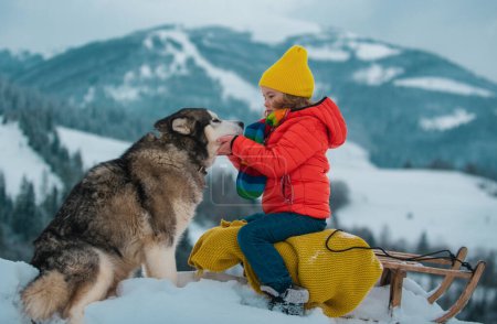 Foto de Retrato de un niño feliz con sombrero de punto, bufanda y suéter con perro husky. Niños abrazando al tierno perro husky. Amor de mascotas - Imagen libre de derechos