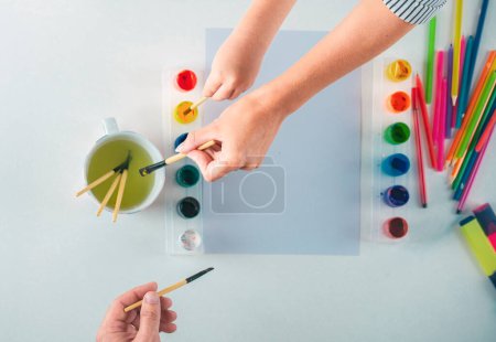 Foto de Escritorio de vista superior de un artista manos con pintura de dibujo pinturas de colores y lápices de colores sobre fondo blanco - Imagen libre de derechos