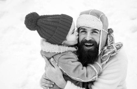 Foto de Feliz hijo de familia abraza a su padre en las vacaciones de invierno. Papá y el niño sonriendo y abrazándose. Feliz Navidad y Feliz Año Nuevo. La mañana antes de Navidad. Feliz padre e hijo - retrato de invierno - Imagen libre de derechos