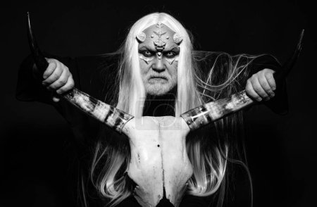Photo for Devil horror concept. Elderly man holding two red horns. Monster with white blue eyes. Viking with a horned head. Alien with dragon skin and grey beard. Evil vampire man - Royalty Free Image