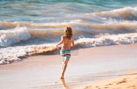 Téléchargez les photos : Vue arrière du garçon enfant sautant et courant sur la plage de la mer - en image libre de droit