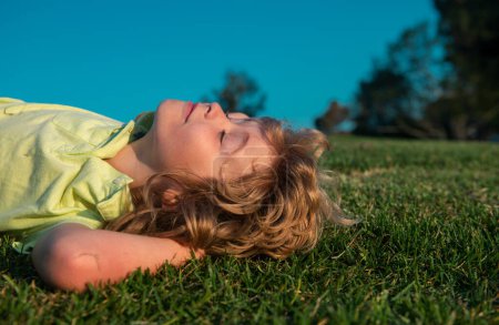 Foto de Niños soñando. Un chico jugando en el prado. Feliz niño caucásico sano con acostado en el fondo del campo de hierba. Niño pequeño en un hermoso entorno verde. Increíble feliz niños al aire libre - Imagen libre de derechos