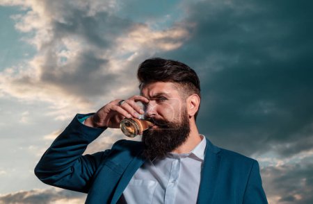 Téléchargez les photos : Un homme barbu tient du cognac de verre. Un barbu boit du cognac. Un homme tenant un verre de whisky. Siroter du whisky. Portrait d'homme à la barbe épaisse. Dégustation, dégustation - en image libre de droit