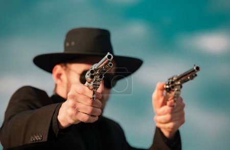 Photo for Sheriff in black suit and cowboy hat shooting gun, close up western portrait. Wild west, western, man with vintage pistol revolver and marshal ammunition - Royalty Free Image