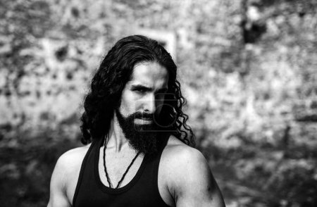 Photo for Young stylish man with determined character. Strong confident man with long wavy dark hair and beard looking at camera. Mans power and confidence concept - Royalty Free Image