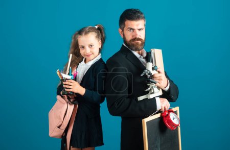 Téléchargez les photos : Père et fille élève prêts pour l'école. Portrait de papa et petites filles avec fournitures scolaires, isolé sur fond bleu - en image libre de droit