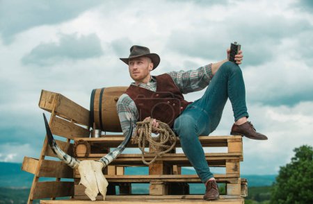 Photo for Guy cowboy. Owner of ranch. Farm worker and farming concept. Handsome man in cowboy hat and rustic style outfit. Guy drinking whiskey - Royalty Free Image