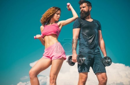 Foto de Pareja de fitness deportiva, hombre barbudo y mujer sexy haciendo ejercicio al aire libre, entrenamiento de pareja deportiva con pesas - Imagen libre de derechos