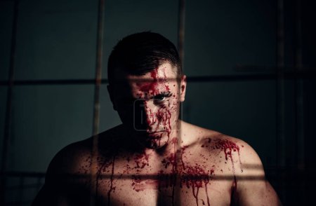 Photo for Halloween concept. Aggressive person. Strong aggressive monster behind grid. Bodybuilder nude torso soiled blood. Prison for monster. Psycho mad man. Psychic disease. Murderer brutal aggressive guy. - Royalty Free Image