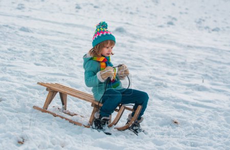 Téléchargez les photos : Garçon glissant avec traîneau dans la neige d'hiver. Vacances pour enfants de Noël et bonne année. Espace de copie arrière-plan neige - en image libre de droit