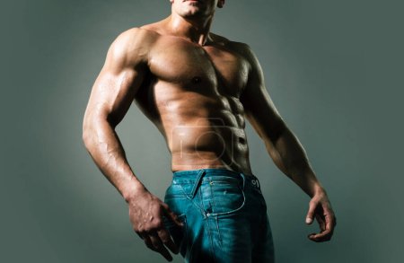 Téléchargez les photos : Sexy muscle homme fort gars en jeans sur fond gris isolé. Corps coupe idéale - en image libre de droit