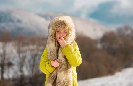 Téléchargez les photos : Petite fille drôle marchant mangeant de la neige le jour d'hiver. Vacances de Noël excitées. Concept pour enfants rhume et grippe - en image libre de droit
