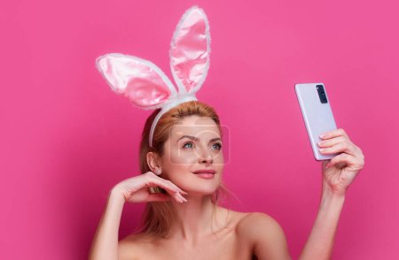 Téléchargez les photos : Jeune femme aux oreilles de lapin. Blogueur tenir le téléphone isolé rose - en image libre de droit