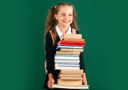 Foto de Día del conocimiento, niña sonriente con mochila sosteniendo libros en pizarra. Concepto de estilo de vida infantil. Educación en la escuela - Imagen libre de derechos