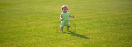 Téléchargez les photos : Bébé sur champ d'herbe printanière, bannière. Enfant en bonne santé. Bébé garçon tout-petit marchant dans un parc le jour du printemps lumineux - en image libre de droit
