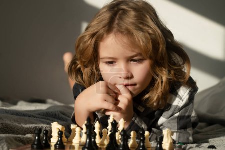Téléchargez les photos : Le petit garçon joue aux échecs à la maison. Intelligent concentré et pensant gamin jouant aux échecs. Enfants développement du cerveau et jeu de logique - en image libre de droit