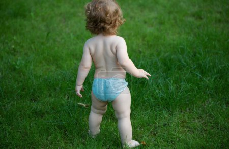 Foto de Vista posterior del bebé de pie descalzo en el césped verde. Feliz infancia y cuidado de niños. Niños creciendo - Imagen libre de derechos