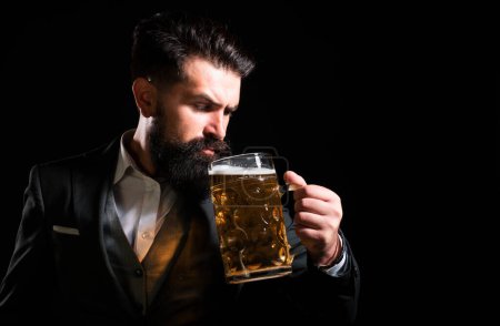 Foto de Hombre retro en traje clásico bebiendo cerveza. barbudo chico satisfecho con levantado alto vaso de cerveza en negro fondo - Imagen libre de derechos
