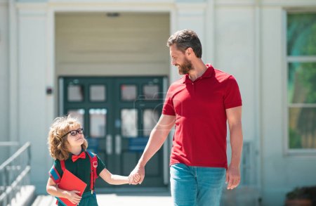 Téléchargez les photos : Père accompagnant son fils à l'école. Parent et élève de l'école primaire écolier avec sac à dos - en image libre de droit