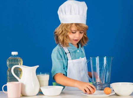 Téléchargez les photos : Portrait de chef enfant en chapeau de cuisinier. Cuisson à la maison, gamin préparant des aliments à partir de légumes et de fruits. Une alimentation saine - en image libre de droit