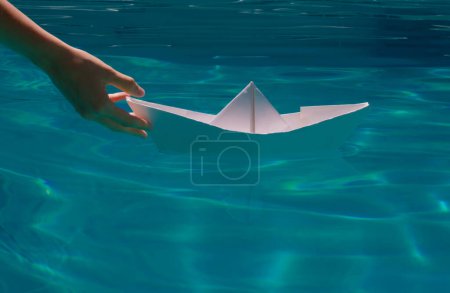 Photo for Hand is launching a white paper boat into the clear sea water. Tourism, travel dreams vacation holiday, dreaming traveling, sailing adventure - Royalty Free Image