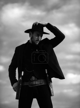 Photo for Sheriff in black suit and cowboy hat. Wild west, western, man with vintage pistol revolver and marshal ammunition - Royalty Free Image