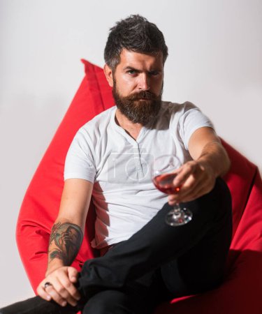 Téléchargez les photos : Un hipster barbu bote un verre de vin. Mauvaises habitudes. Boire de l'alcool. Parti à la maison - en image libre de droit