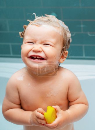 Foto de Sonriendo hermoso bebé bañándose en la ducha. Divertido bebé niño bañado en espuma y lavado en la bañera en casa - Imagen libre de derechos