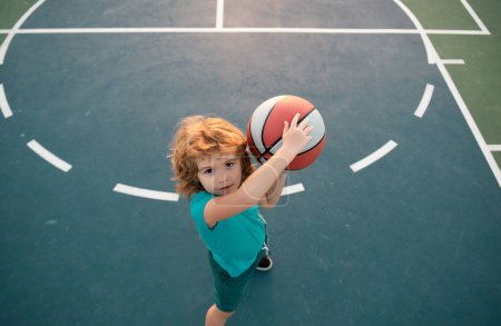 Téléchargez les photos : Mignon petit garçon tenant une balle de basket essayant de faire un score. Sport pour enfants, Vue de dessus - en image libre de droit