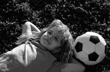 Téléchargez les photos : Garçon de football rêvant, allongé sur l'herbe. Mignon petit enfant rêve de devenir un joueur de football - en image libre de droit