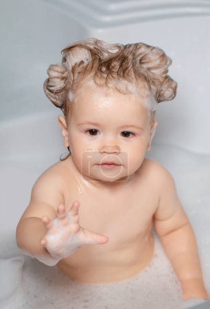 Téléchargez les photos : Enfant sous la douche. Bébé enfant se lave dans une salle de bain en mousse. Enfant dans la baignoire avec bulle de savon moelleux - en image libre de droit