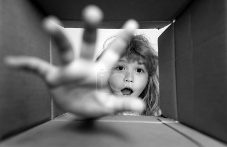 Foto de Niño niño abriendo una caja de cartón y mirando dentro, tomar a mano regalo. Concepto de desempaquetado, sorpresa de desempaquetado. Parcelas y entrega - Imagen libre de derechos