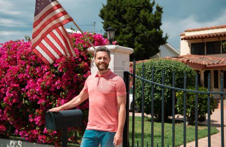 Téléchargez les photos : Agent immobilier souriant près d'une nouvelle résidence à vendre, à l'extérieur. Louer une nouvelle maison avec drapeau amarican - en image libre de droit