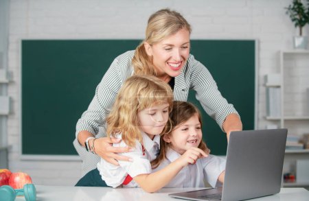 Photo for Kids learning with teacher. Children from elementary school study at lesson. Boy and girl with teacher learn english language or mathematics on laptop. Education and knowledge - Royalty Free Image