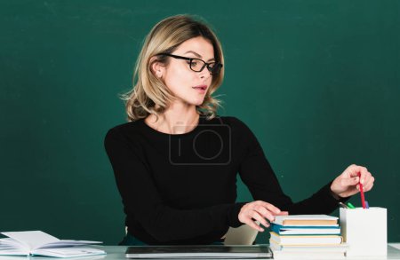 Photo for Modern attractive teacher. Portrait of smart young woman in glasses with book on the blackboard in class at high school or collage. Education and tutoring concept - Royalty Free Image