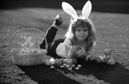 Téléchargez les photos : Enfants célébrant Pâques peinture oeufs. Enfant en costume de lapin avec oreilles de lapin en plein air - en image libre de droit