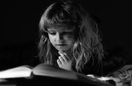 Foto de Feliz infancia, niño soñador. Niño leyendo un libro en la cama antes de irse a dormir. Niño tendido en la cama leyendo libro en casa - Imagen libre de derechos