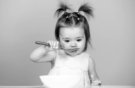 Photo for Baby food, babies eating. Portrait of cute Caucasian child kid with spoon. Hungry messy baby with plate after eating puree - Royalty Free Image