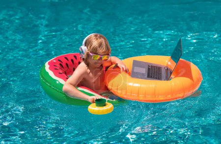 Photo for Summer office and freelance concept. Little business man relaxing in the pool with laptop. Kid online working on laptop, swimming in a sunny turquoise water pool - Royalty Free Image