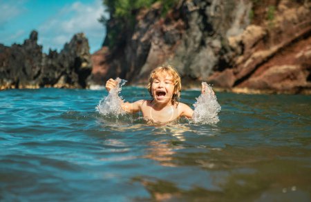 Téléchargez les photos : Enfant jouant dans l'eau de mer. Il saute dans les vagues de la mer. Vacances d'enfants sur la plage. Petit garçon excité nageant pendant les vacances d'été - en image libre de droit