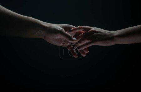 Téléchargez les photos : Deux mains s'étirent, fond noir. Couple amoureux tenant des mains, gros plan. Aide main, soutien, amitié - en image libre de droit